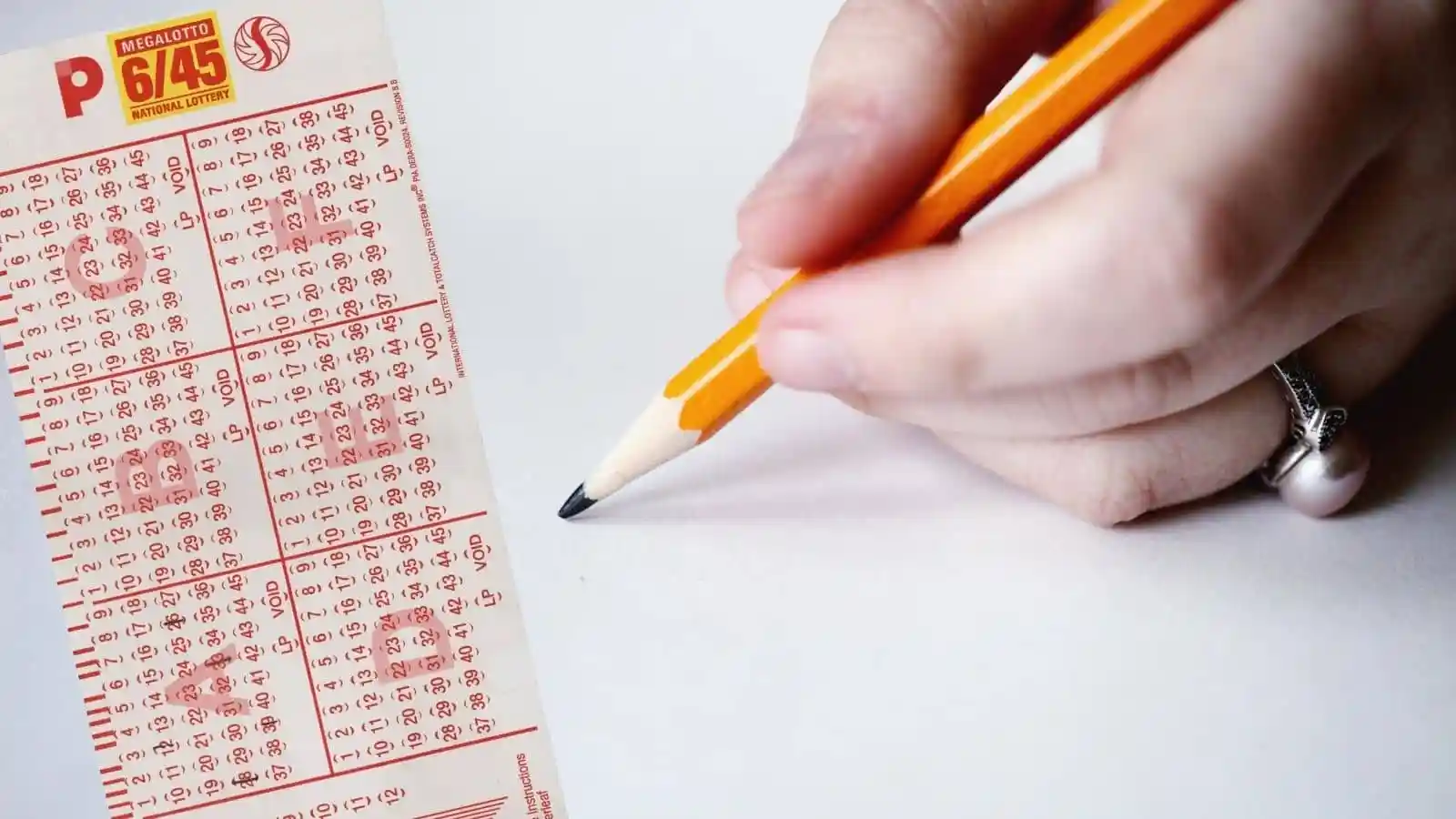 hand with ring holding yellow pencil matching numbers on pcso national lottery mega lotto ticket