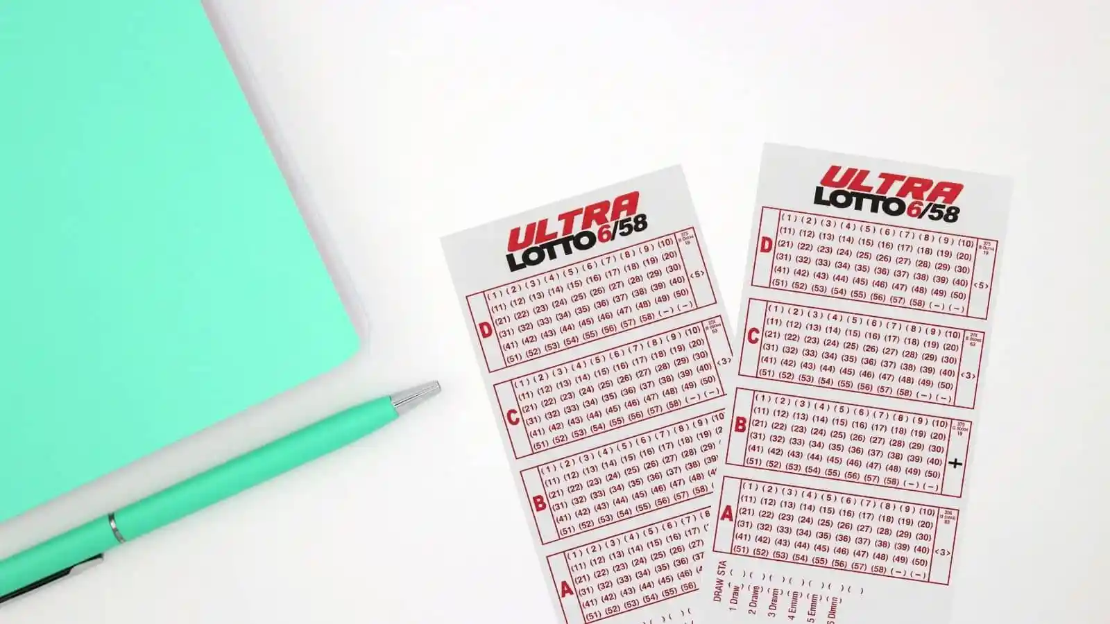 green notebook, green pen and ultra lotto pcso tickets on white board seen from above